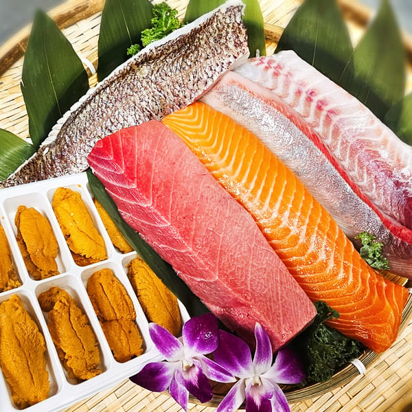 Assortment of fresh tuna, salmon, sea bream, and uni on a bamboo platter with green leaves and orchids.