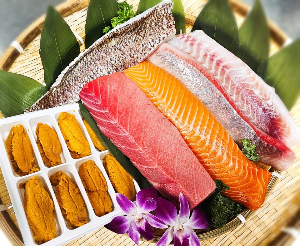Assortment of fresh tuna, salmon, sea bream, and uni on a bamboo platter with green leaves and orchids.