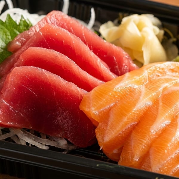 Fresh salmon and tuna sashimi with shredded daikon, ginger, and wasabi in a black container.